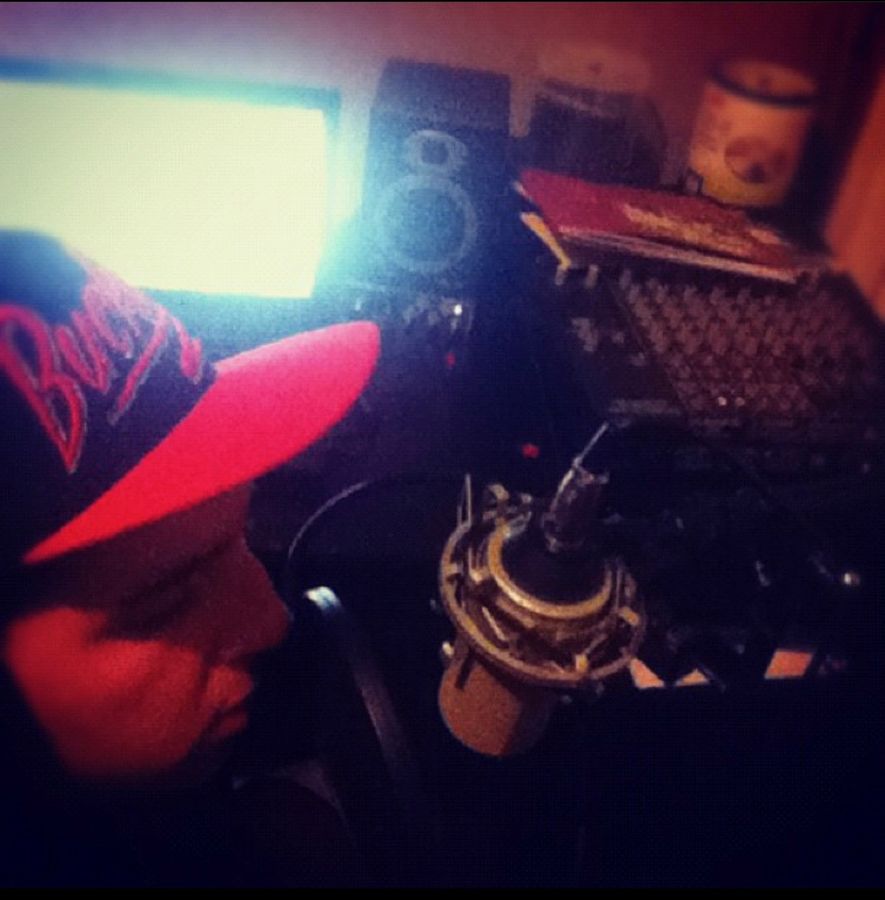 Recording at the mic in a red snapback, monitors and a mixer in the background